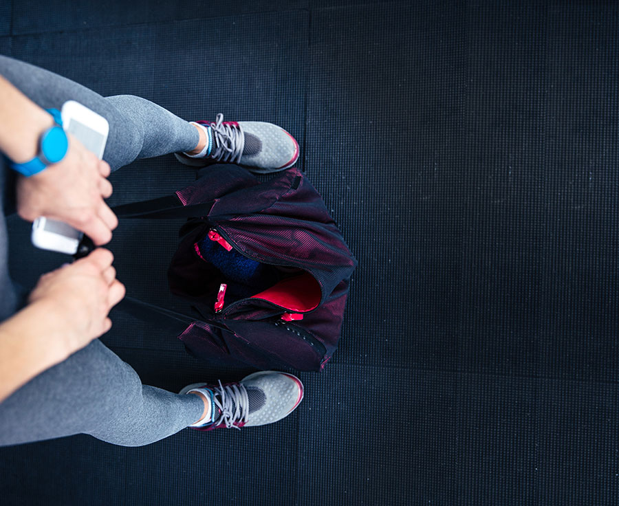 woman-holding-cellphone-gym-bag-on-the-floor